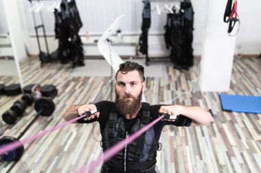 Genç sakallı adam elektriksel kas stimülasyonu elbisesi üzerinde egzersiz yapıyor..