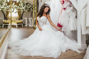 Çekici genç esmer kadın gülümseyip eğlenirken modern düğün salonundaki gelinliği seçiyor..