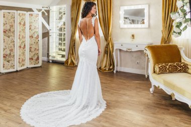 Çekici genç esmer kadın gülümseyip eğlenirken modern düğün salonundaki gelinliği seçiyor..