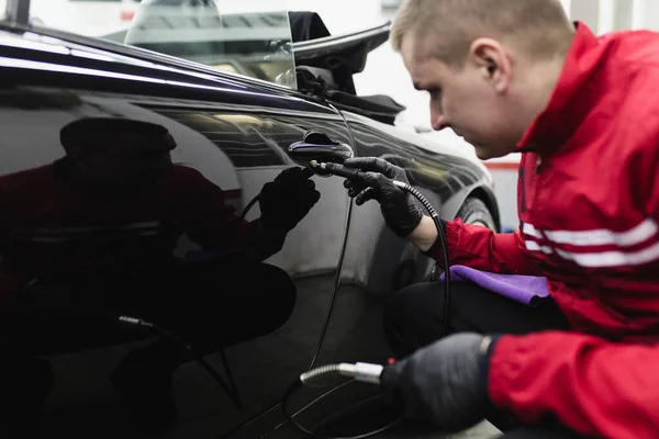 Car detailing, worker with orbital polisher in auto repair shop.