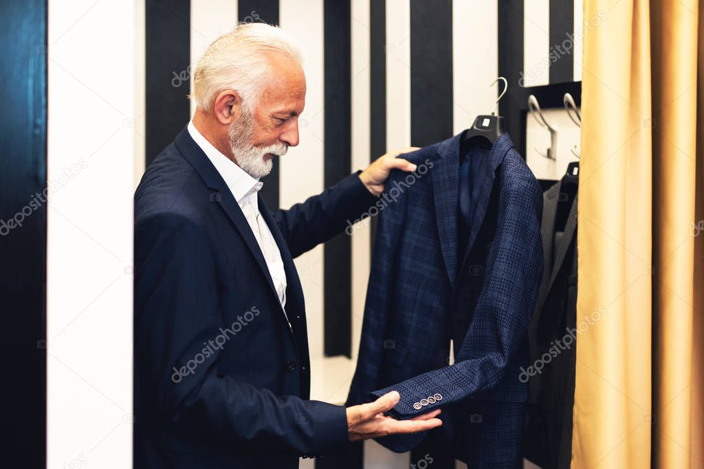 Stylish and modern senior business man choosing and buying suite in expensive store