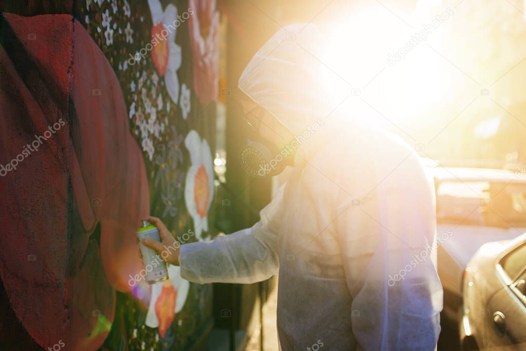 Young graffiti artist painting mural outdoors on street wall.