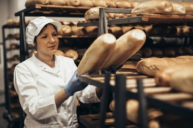 Fırında çalışan ve raflara ekmek koyan genç bir bayan işçi.