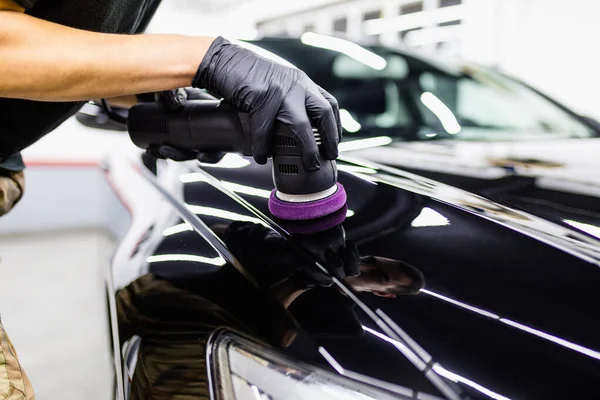 Car detailing, worker with orbital polisher in auto repair shop.