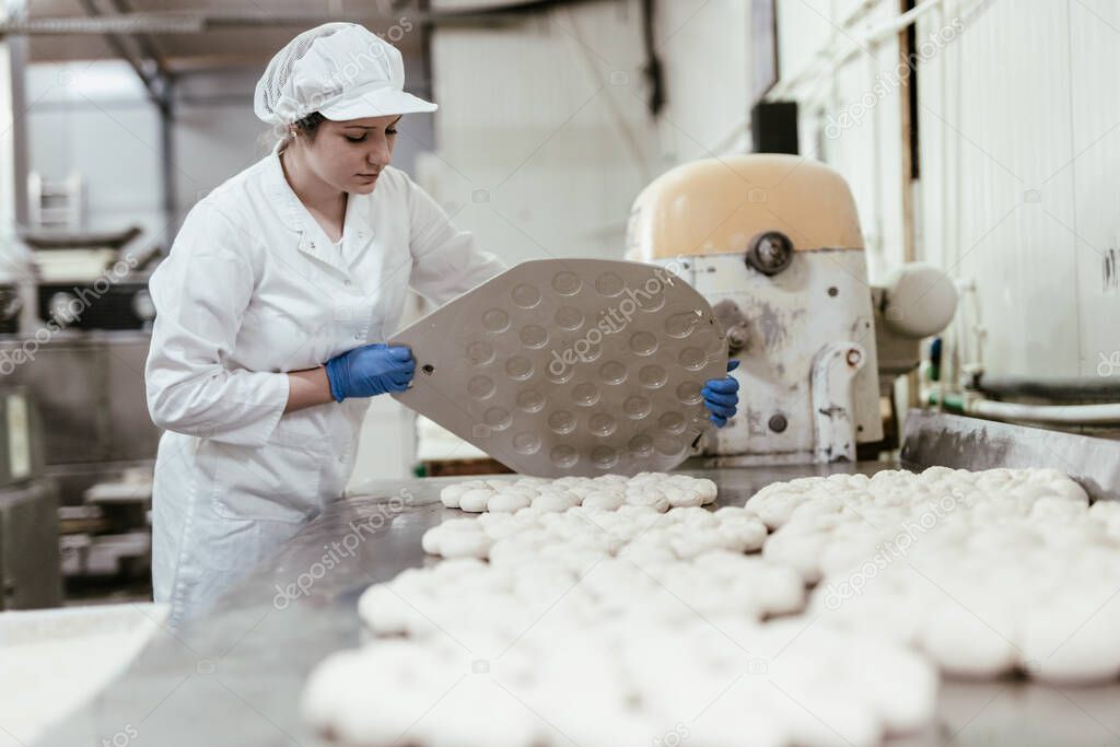 Young female worker working in large bakery. Bread preparation.