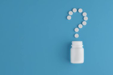 İlaç hapları ve bir şişe mavi bir arka plan üzerinde. Kavram soru işareti