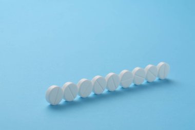 Satırda mavi zemin üzerine dizilmiş tabletleri. Kavram dozaj, aşırı doz, düzenlilik, uyum