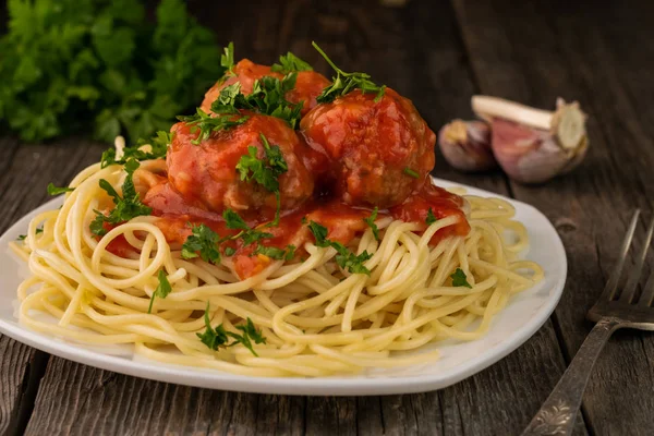 Close-up de espaguete americano com almôndegas e molho de tomate com alho e cebola em um fundo de madeira rústico — Fotografia de Stock