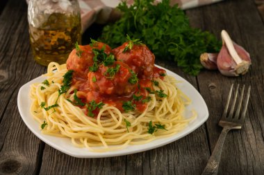 Domates soslu köfteli bir tabak spagetti ve arka planda pişirmek için bazı malzemeler.