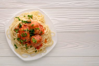 Domates soslu köfteli spagetti ve beyaz ahşap arka planda maydanoz.