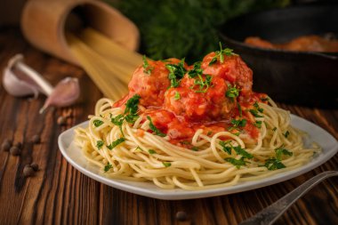 Domates soslu köfteli bir tabak spagetti ve arka planda kızartma tavalı çiğ spagetti.