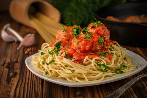 Close-up um prato de espaguete com almôndegas em molho de tomate e espaguete cru com uma frigideira no fundo — Fotografia de Stock