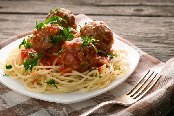 Close up plate of spaghetti with meatballs in tomato sauce sprinkled with parsley on table-napkin on wooden rustic table — Stock Photo, Image