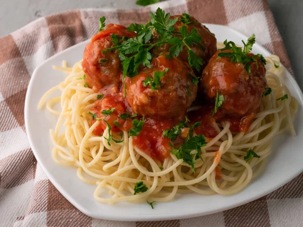 Closeup cooked spaghetti with meatballs in tomato sauce on a checkered cotton table-napkin on wooden background — Stock Photo, Image