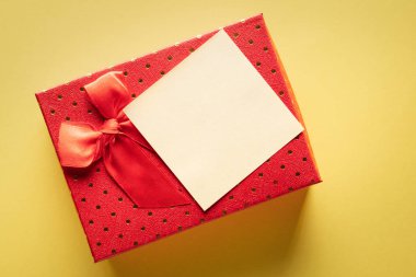 Sarı arka planda boş bir notla kırmızı hediye kutusunu kapat: hediye verme veya hatırlatma kavramı