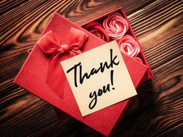 Geschenkbox mit Knospen von dekorativen Rosen im Inneren und einem Zettel mit der Aufschrift "Danke" auf einem hölzernen Hintergrund: das Konzept des Gebens und Ausdrucks von Dankbarkeit — Stockfoto