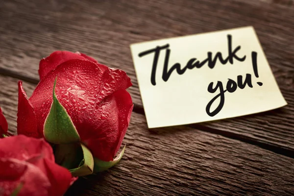 Nahaufnahme einer Rosenknospe und eines Zettels mit der Aufschrift "Danke!" auf hölzernem Hintergrund: Konzept des Ausdrucks der Dankbarkeit — Stockfoto