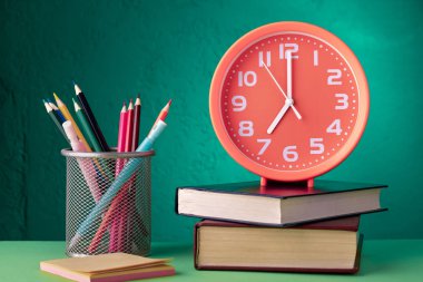 Alarm saati saat yedide bir sepetin içinde kitap ve kalemlerin üzerinde duruyor: okula dönüş konsepti
