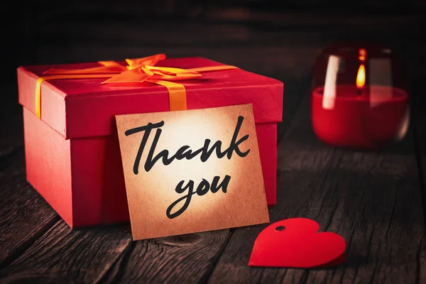 Ein Zettel mit der Aufschrift "Danke" neben einer roten Geschenkschachtel und einer brennenden Kerze: ein Weihnachtsgeschenkkonzept oder ein Ausdruck der Dankbarkeit — Stockfoto