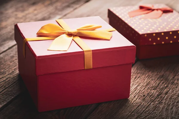 Nahaufnahme rote Geschenkschachtel mit einem gelben Band, das mit einer Schleife auf einem hölzernen Hintergrund gebunden ist: Konzept eines Urlaubs oder eines romantischen Geschenks — Stockfoto