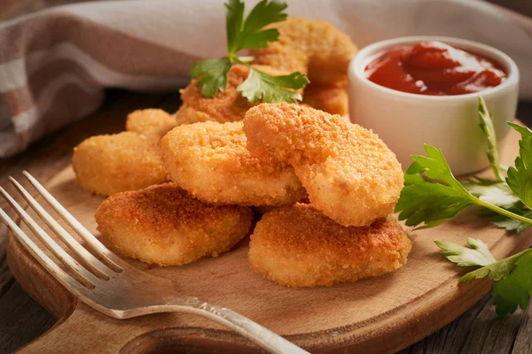 Close-up de nuggets de frango em uma placa em uma placa de corte com molho de tomate chili e salsa em um fundo de madeira — Fotografia de Stock