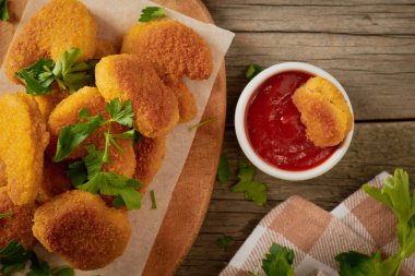 Maydanoz yapraklı tavuk nuggetları kesme tahtasının üzerinde ve domates soslu nugget dilimleri.