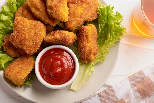 Nuggets de pollo en rodajas en ketchup en un plato con un montón de nuggets y una copa de vino — Foto de Stock
