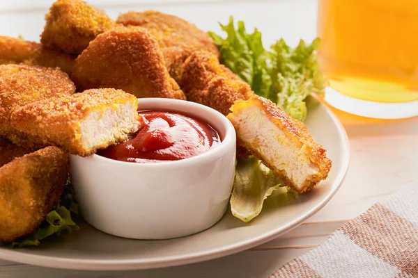 Close-up de uma fatia de nuggets de frango em ketchup em um prato com um monte de nuggets com vinho de vidro — Fotografia de Stock