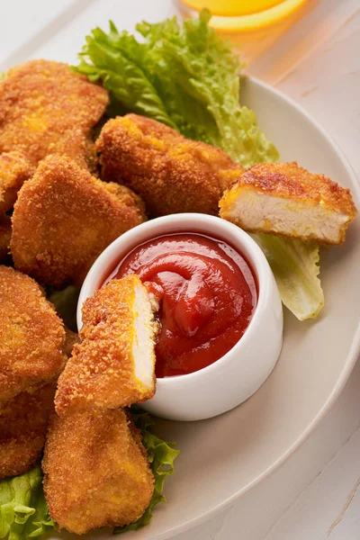 Cerrar rebanada de nuggets de pollo en ketchup en un plato con una pila de nuggets tiro vertical — Foto de Stock