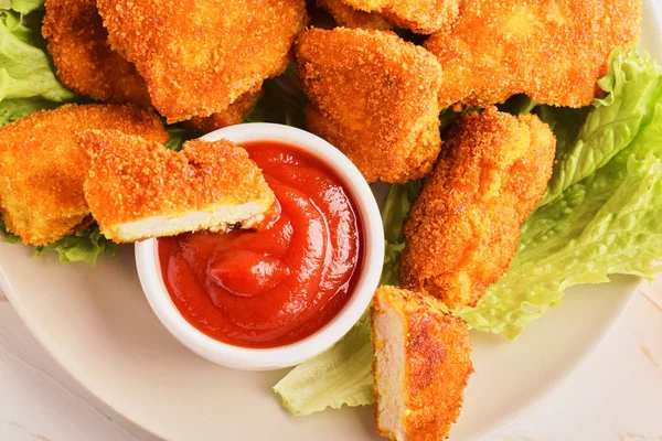 Top view sliced chicken nuggets in ketchup in a plate with a bunch of nuggets and lettuce