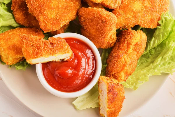 Ovanifrån skivade kycklingnuggets i ketchup i en tallrik med ett gäng nuggets och sallad — Stockfoto