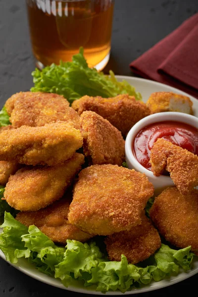 Um prato de nuggets de frango cozido com ketchup e um copo de cerveja em um fundo escuro. Quadro vertical — Fotografia de Stock