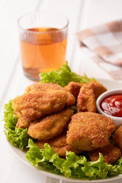 Nuggets de pollo con salsa de tomate y lechuga en un plato sobre un fondo de madera blanca. Disparo vertical — Foto de Stock