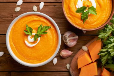 İki kâse balkabağı çorbası ve ahşap arka planda kesme tahtasındaki çiğ balkabağı manzarası.