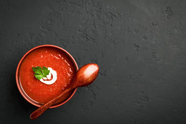 コピースペースのある暗い背景に木製のスプーンで茶色のボウルにトマトスープをトップビュー — ストック写真