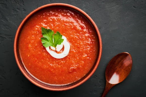 Vista superior close-up de uma tigela marrom de sopa de tomate com salsa e creme de leite e uma colher de madeira em um fundo escuro — Fotografia de Stock