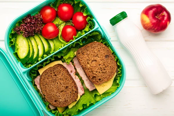 Top view of school lunch box with sandwiches and vegetables and a bottle of yogurt: a concept of healthy and balanced nutrition.