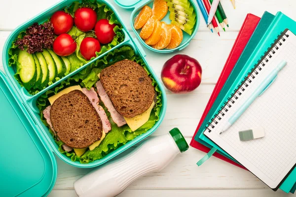 School lunch box with sandwiches and fruit vegetables and school supplies: the concept of a healthy and balanced diet.