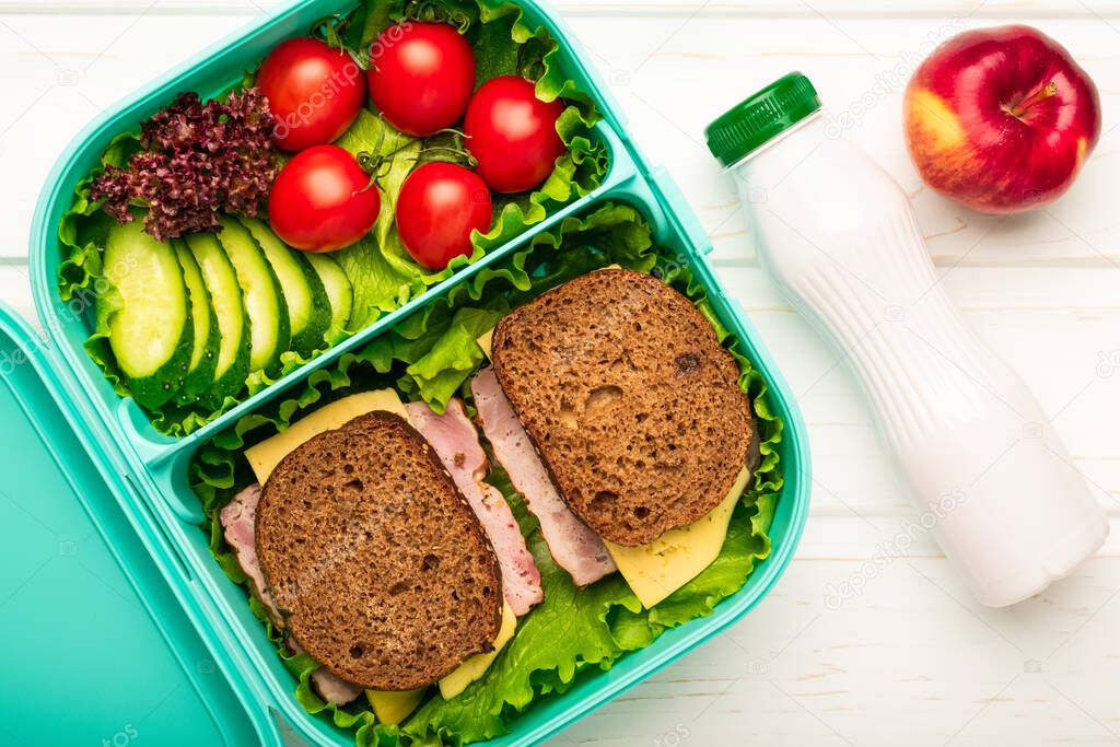 Top view of school lunch box with sandwiches and vegetables and a bottle of yogurt: a concept of healthy and balanced nutrition.