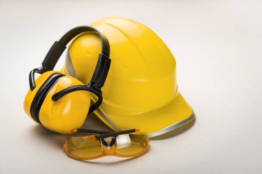 Hafif arka planda gözlüklü sarı başlık ve kulaklıklar: kişisel sağlık ve güvenlik ekipmanları kavramı.