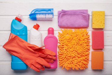 Beyaz ahşap arka planda genel temizlik için malzeme ve kimyasalların üst görünümü.