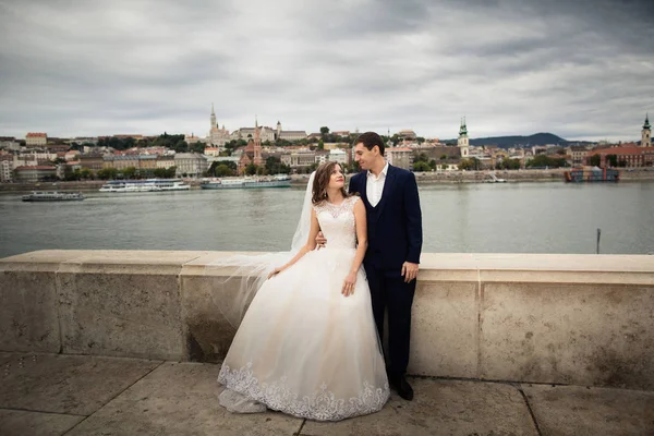 Pengantin pria dan wanita berpelukan di jalan kota tua. Pasangan pernikahan berjalan di Budapest dekat Gedung Parlemen. Pengantin pria dan wanita di dekat sungai . — Stok Foto