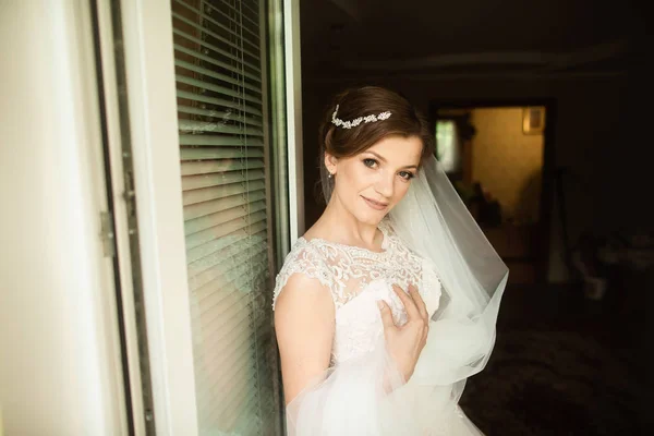 Piękny styl panny młodej. Ślub dziewczyna stoją w luksusowej sukni ślubnej w pobliżu okna — Zdjęcie stockowe