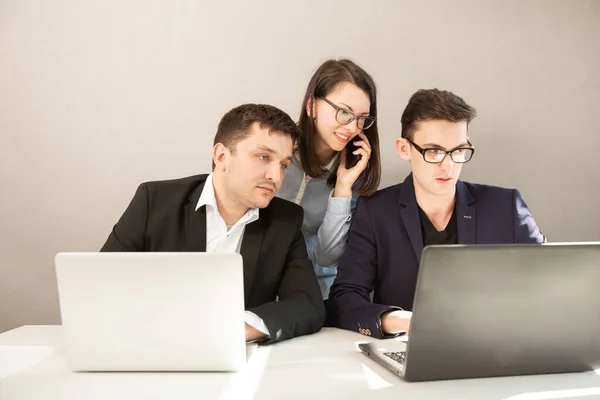 Young male and female business partners sitting behind a computer monitor. Focused business team working, woman talking on mobile phone.