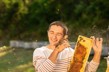 Arıcı arılarla dolu bir bal peteği tutuyor. Gülümseyen ve yüzünde arılarla elini yavaşça dinlendiren bir adam..
