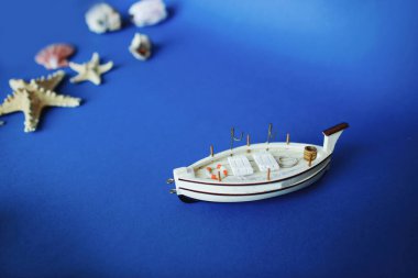 Mavi arka planda deniz kabukları olan beyaz oyuncak gemi. Seyahat ve yaz tatili konsepti. Boşluğu kopyala.