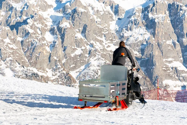 A lifeguard rides a snowmobile with a sleigh along the ski slope against the background of the dolomites. Concept profession, sport. — Stock Photo, Image