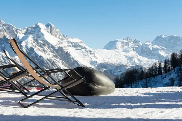 Cadeiras de praia vazias estão na neve contra o pano de fundo de montanhas cobertas de neve. O conceito de férias, paisagem . — Fotografia de Stock