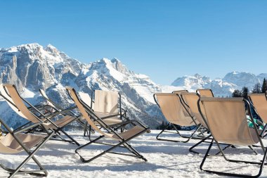 Boş güverte sandalyeleri kar örtülü dağların arka planına karşı karın üzerinde duruyor. Tatil konsepti, manzara