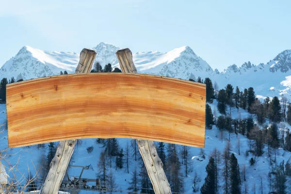 Blank billboard for outdoor advertising from logs and a wooden board on a ski slope against a background of snow-capped mountains and sky. The concept of advertising, landscape, skiing.